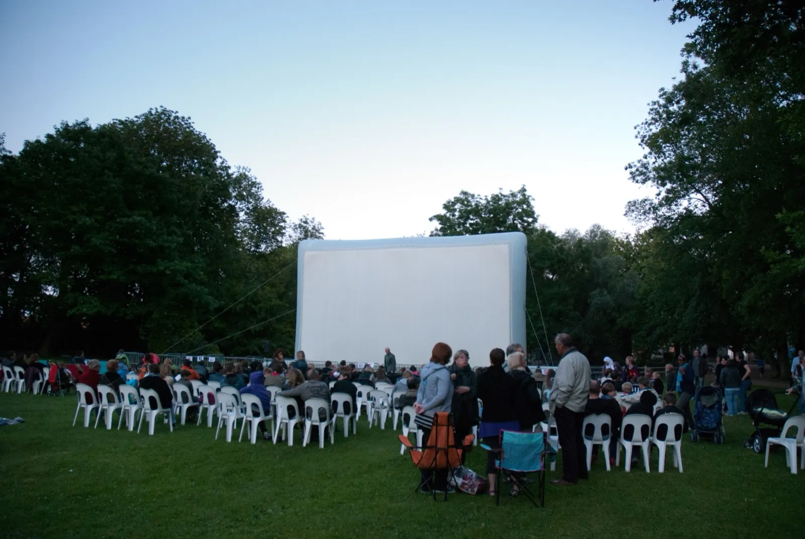 Écran de cinéma gonflable géant Hallucine installé dans un parc, public installé à la tombée du jour