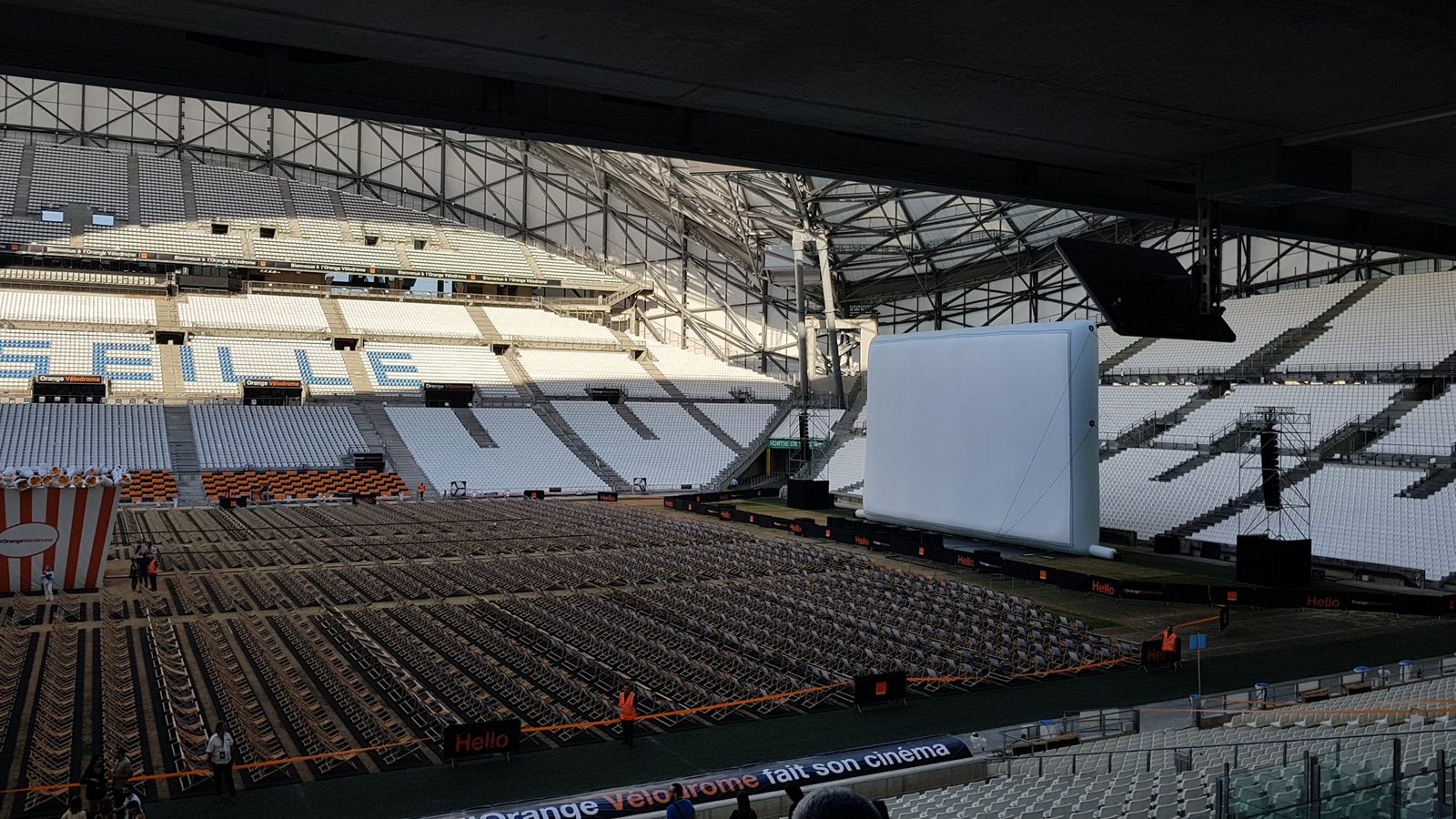 Grand écran gonflable blanc à la silhouette lisse installé sur la pelouse d'un stade vide avec des chaises alignées face à la scène.